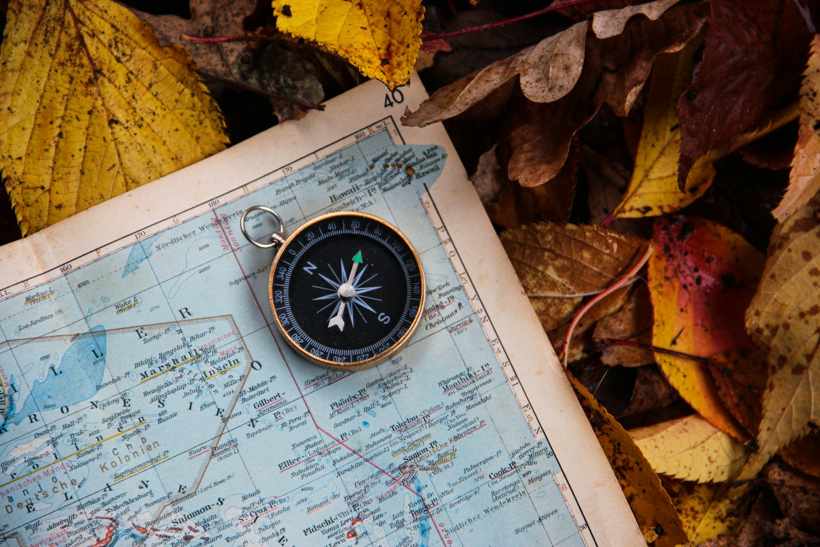 Old compass lying on a map among autumn leaves