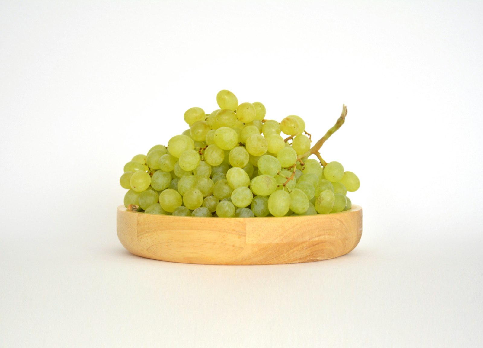 Un cuenco de madera lleno de uvas verdes